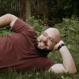 A picture of Brian LaClair laying in the grass with a flower in his mouth, smiling